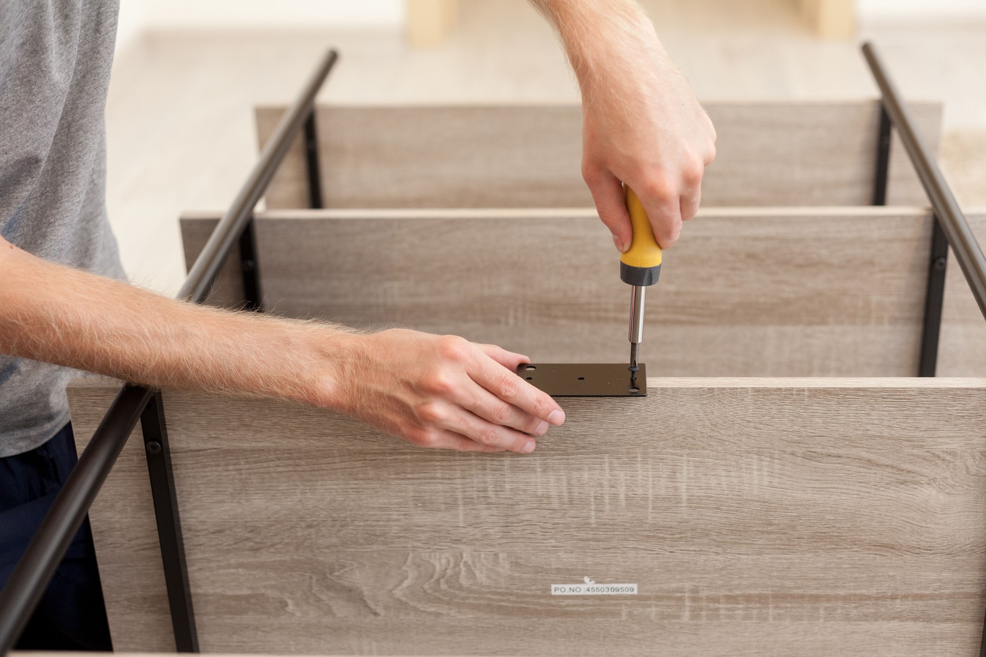 The handyman twists the bolt on the shelf of the bookcase with a screwdriver.