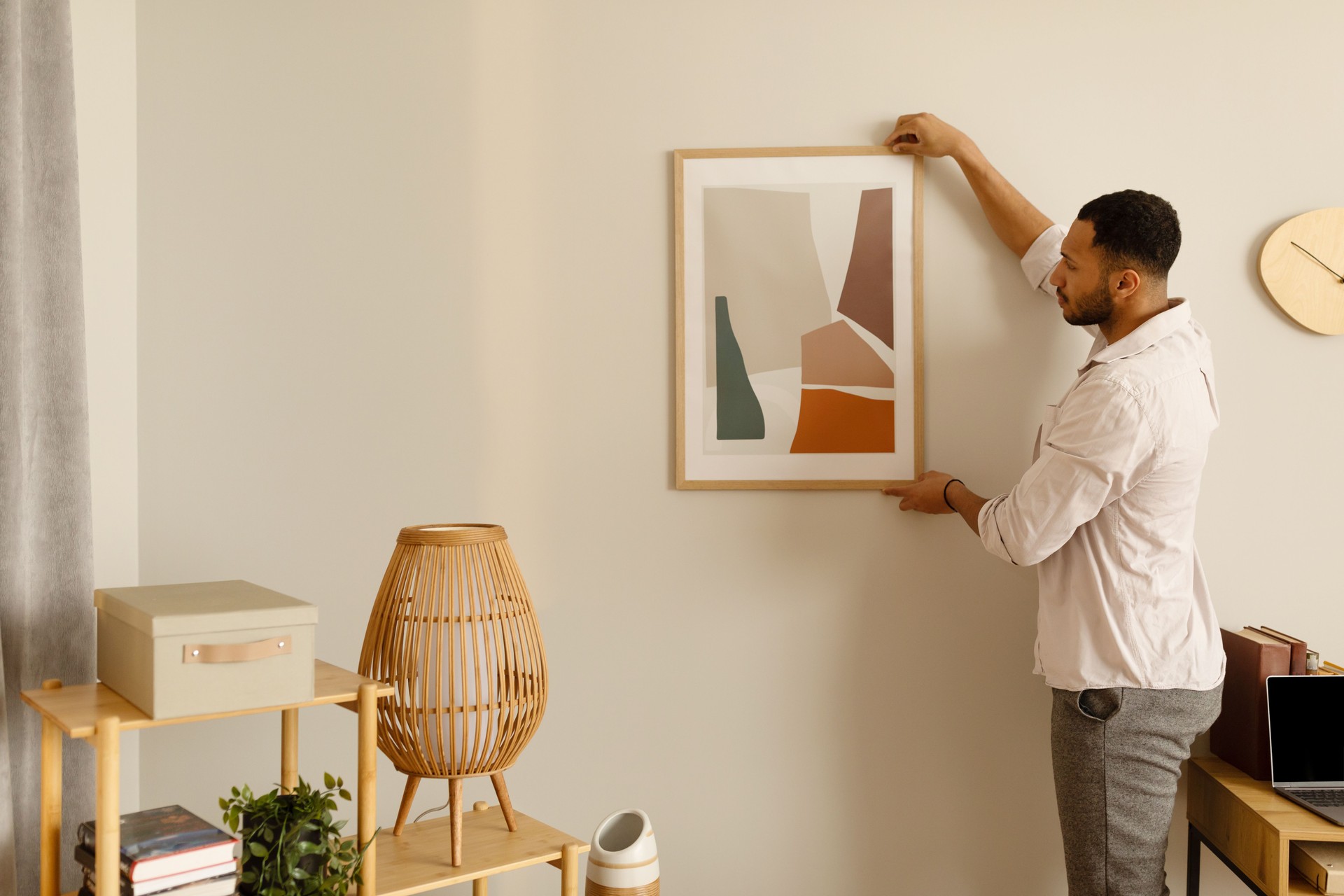 Modern home decor and interior design. Young black man hanging painting, putting picture frame on wall indoors